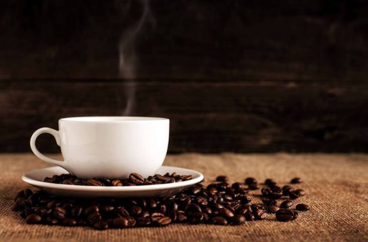 steaming cup of coffee with toasted coffee beans